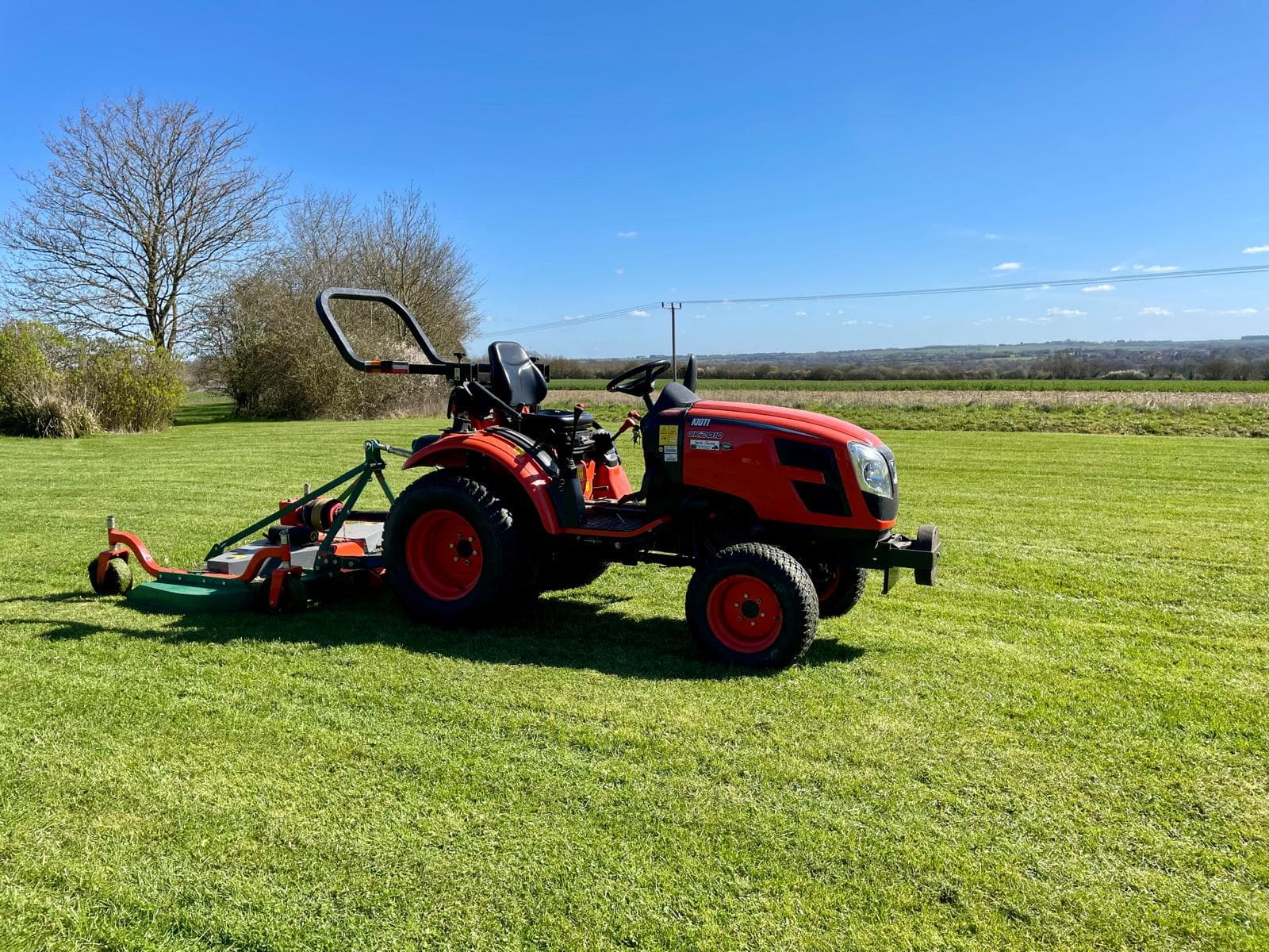 A compact tractor with a mounted finishing mower on a large freshly cut field, with open countryside behind